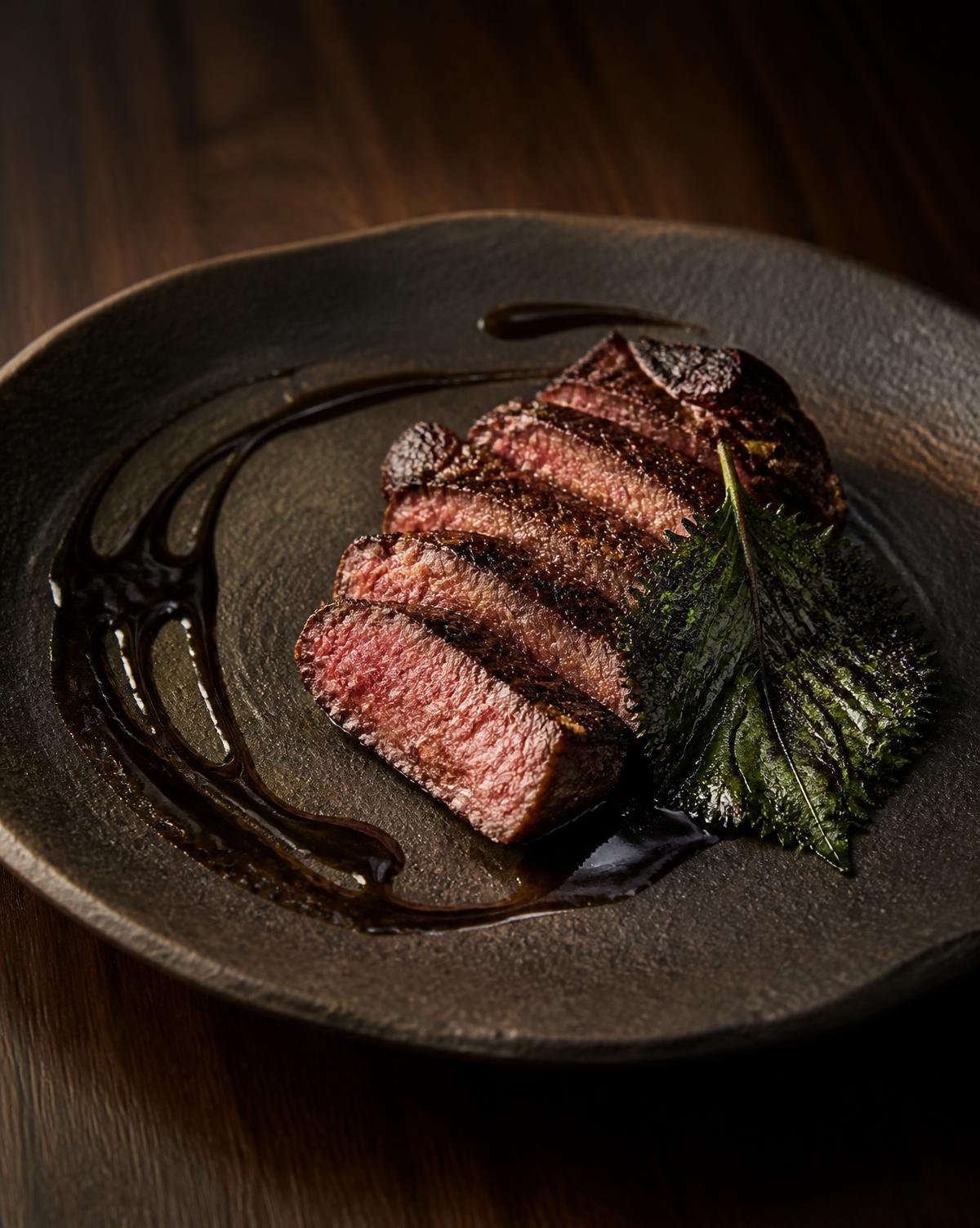 Charcoal-grilled dry-aged hanwoo beef with black garlic jus on dark ceramic